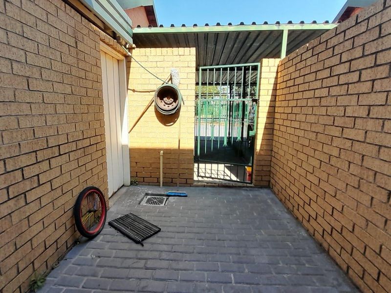A paved rear courtyard area enclosed by brick boundary walls, featuring a metal security gate and a covered section.