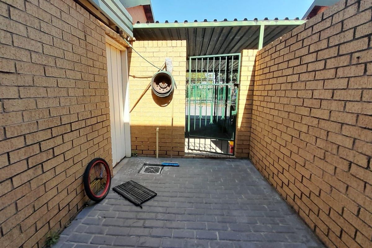 A paved rear courtyard area enclosed by brick boundary walls, featuring a metal security gate and a covered section.