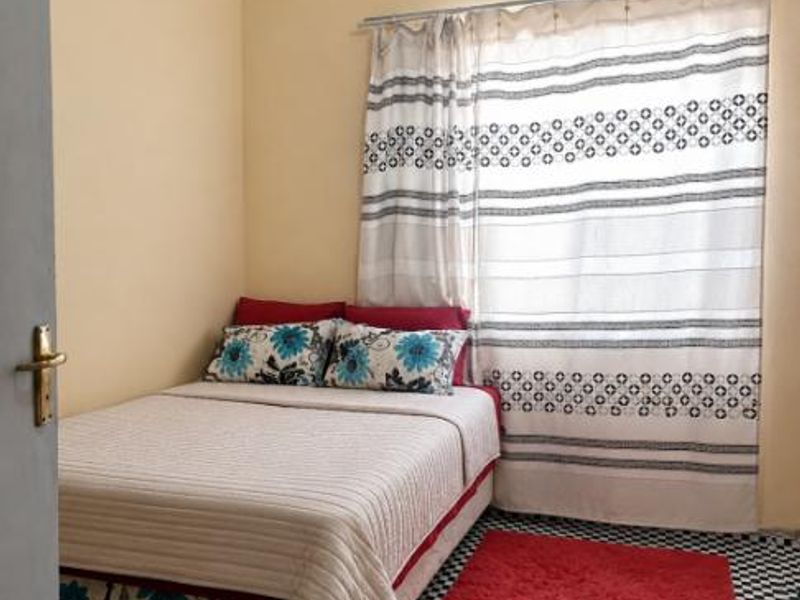A compact bedroom featuring tiled flooring and a window with a fitted curtain rod.