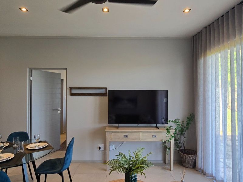 A bright and modern living area featuring tiled floors, recessed lighting, a ceiling fan, and large sliding glass doors providing ample natural light.