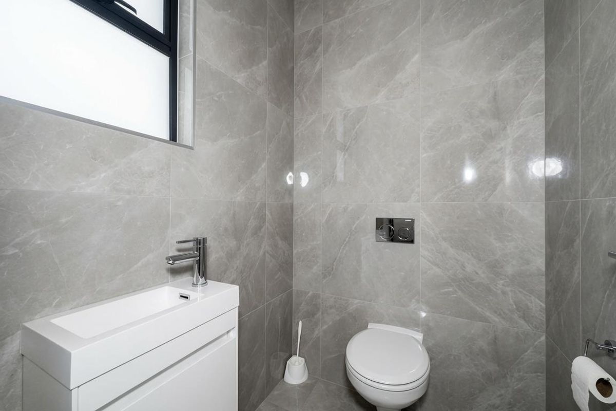 Modern guest bathroom featuring floor-to-ceiling grey marble-look tiles, a wall-mounted toilet with concealed cistern, and a sleek vanity basin.