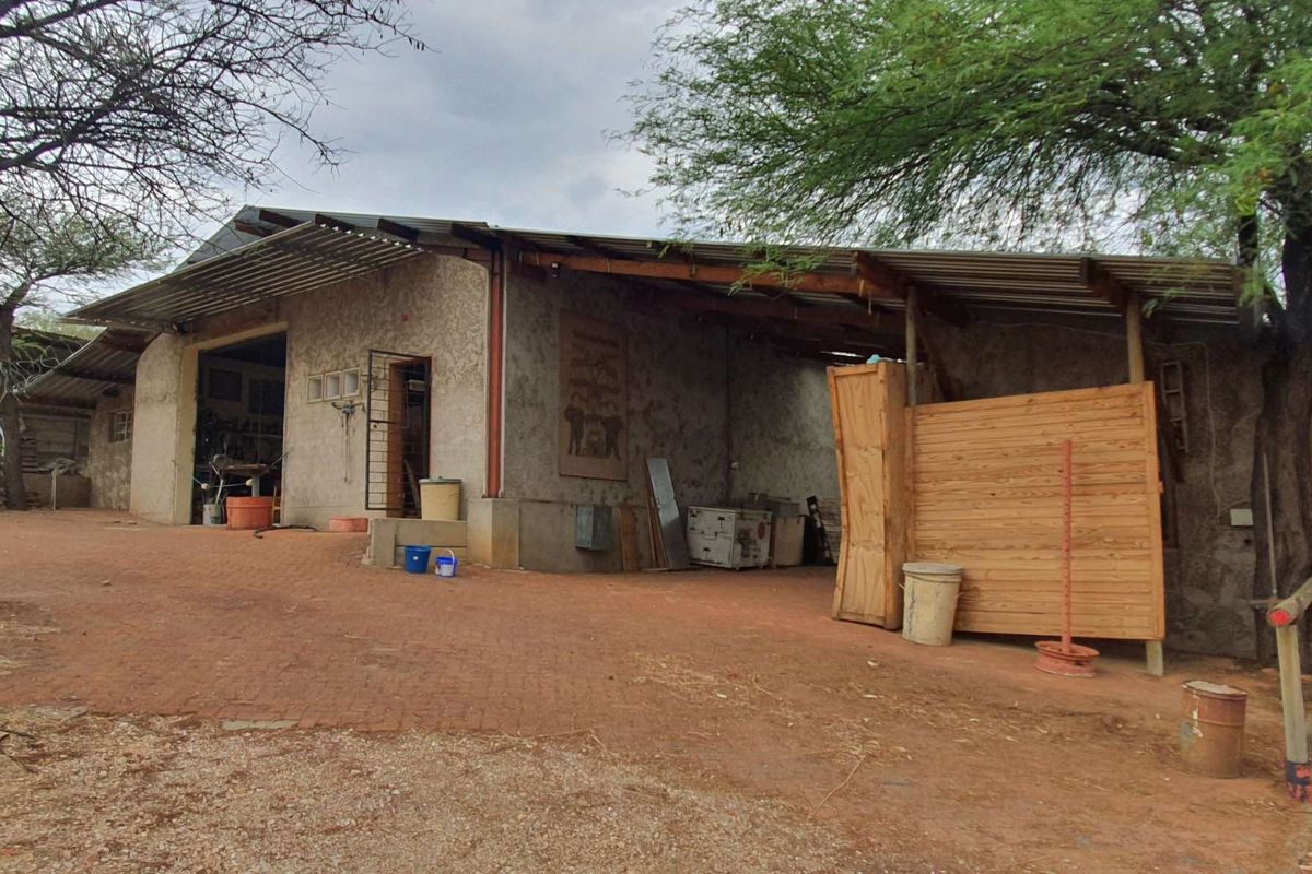 Exterior view of a rustic outbuilding or utility structure featuring a corrugated metal roof, rough-cast walls, and an attached covered workspace area.