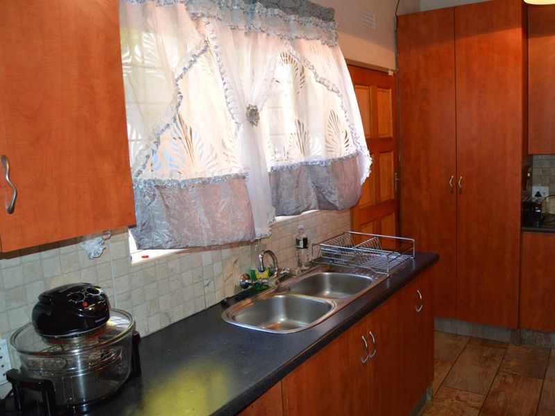 A functional kitchen featuring wood-look laminate cabinetry, a double stainless steel sink, tiled backsplash, and durable tiled flooring.