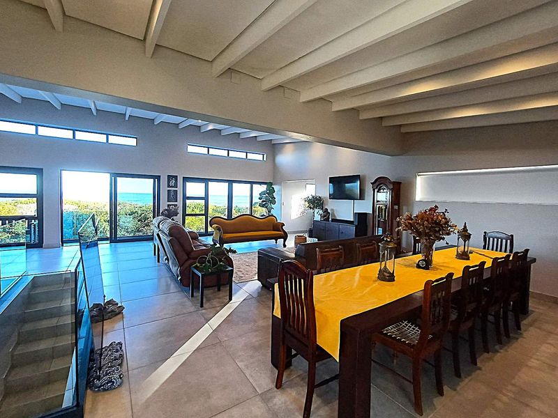 Spacious open-plan living and dining area featuring high exposed beam ceilings, large format floor tiles, and expansive sliding glass doors with ocean views.