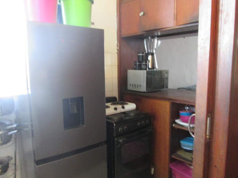 A compact kitchen area featuring dated wooden cabinetry, a tiled backsplash, and space for a freestanding stove.