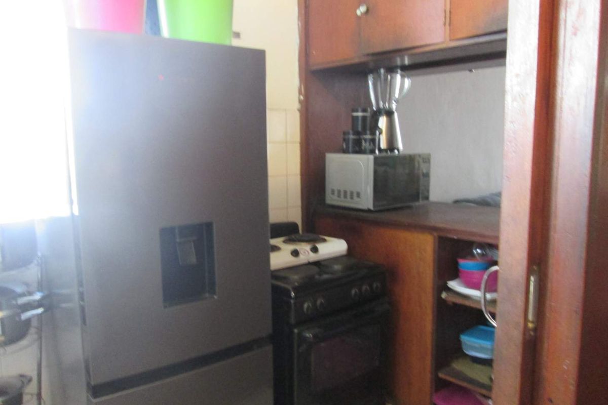 A compact kitchen area featuring dated wooden cabinetry, a tiled backsplash, and space for a freestanding stove.