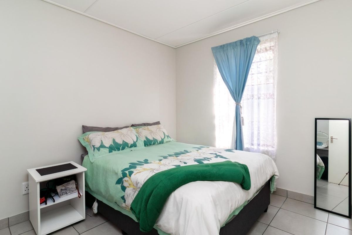 A functional bedroom featuring tiled flooring and a window with security bars, providing a simple and practical living space.