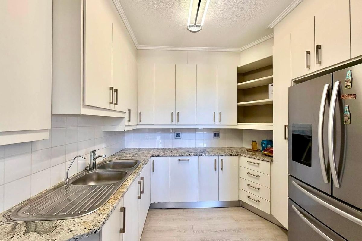 A functional kitchen featuring white cabinetry, granite countertops, a double stainless steel sink, and a tiled backsplash with ample storage space.