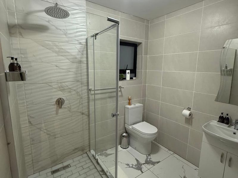 Modern bathroom featuring a walk-in shower with glass enclosure, marble-look tiled walls and floors, a vanity basin, and a toilet.