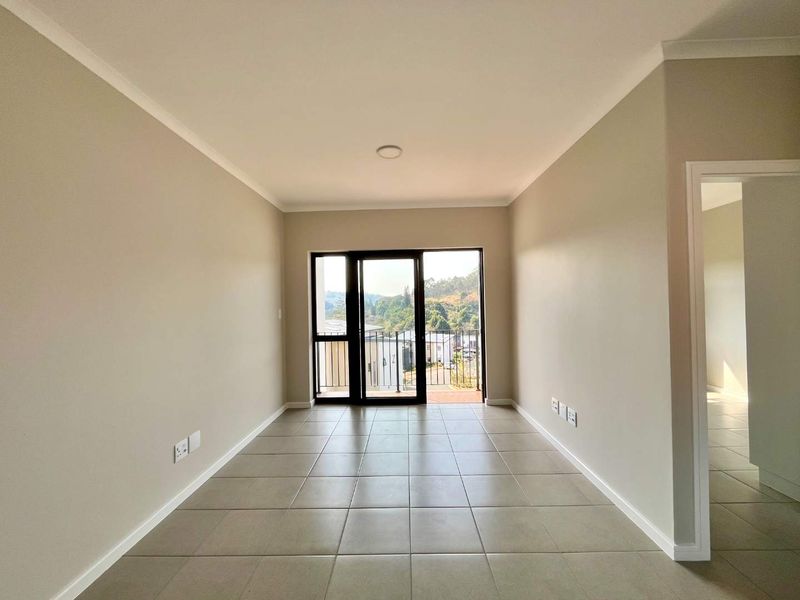A bright, empty living area featuring neutral tiled floors, clean walls, and a sliding glass door providing access to a balcony with scenic views.