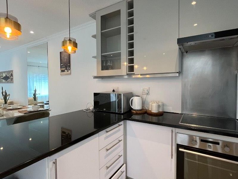 Modern kitchen featuring sleek white cabinetry, black granite countertops, integrated stainless steel appliances, and contemporary pendant lighting.