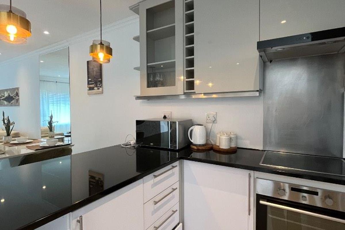 Modern kitchen featuring sleek white cabinetry, black granite countertops, integrated stainless steel appliances, and contemporary pendant lighting.