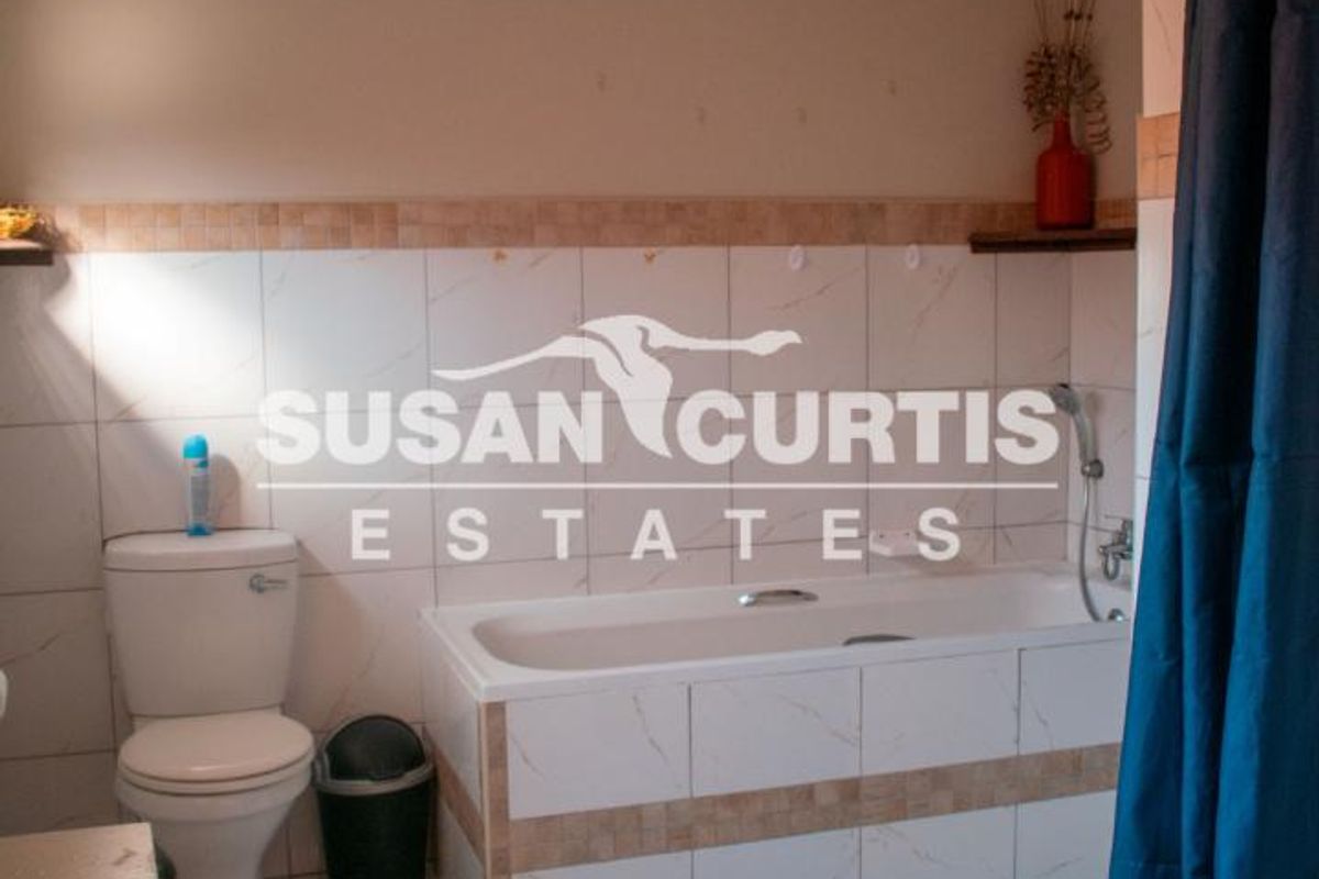 A functional bathroom featuring a bathtub with shower mixer, toilet, and neutral tiled finishes throughout.