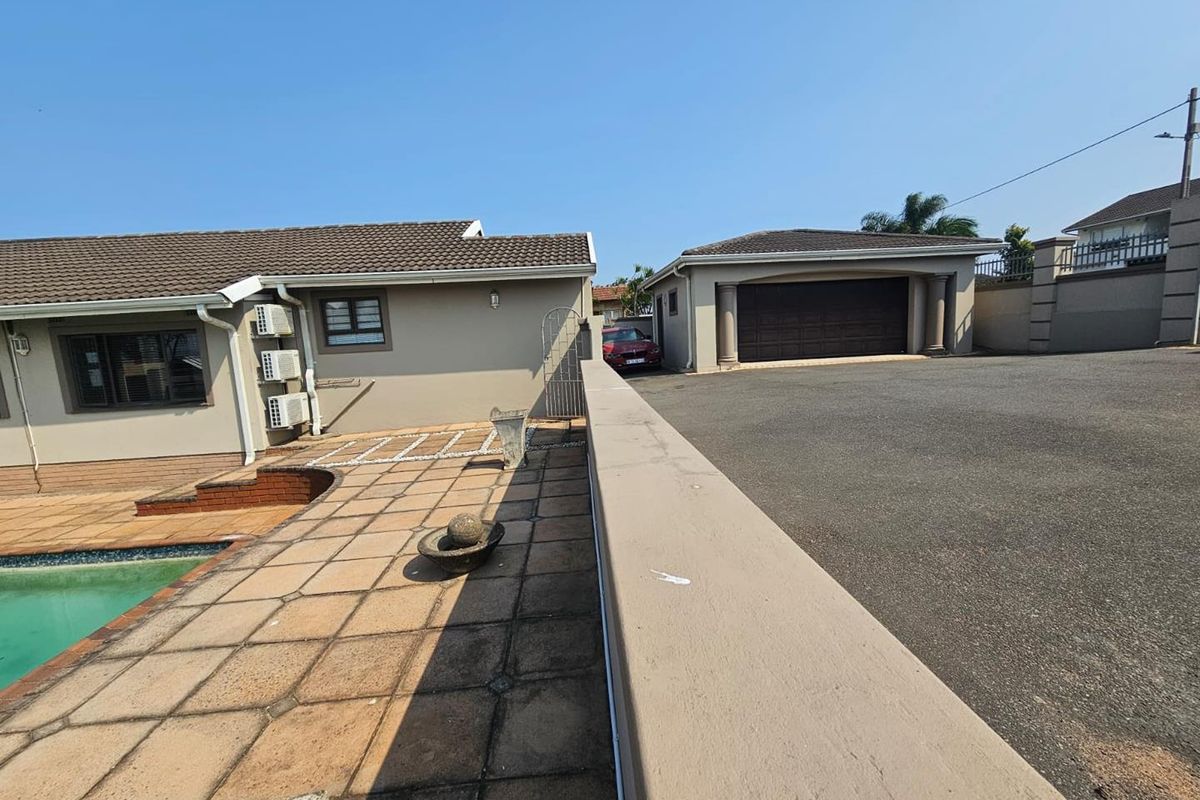 Rear exterior view featuring a tiled patio area, swimming pool, and a detached double garage with an asphalt driveway.