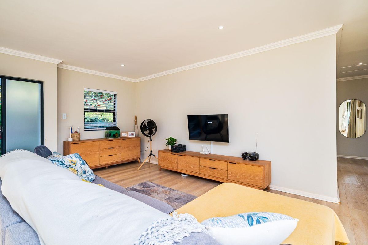 A bright and well-maintained living room featuring modern laminate flooring, recessed downlighting, and elegant ceiling cornicing.