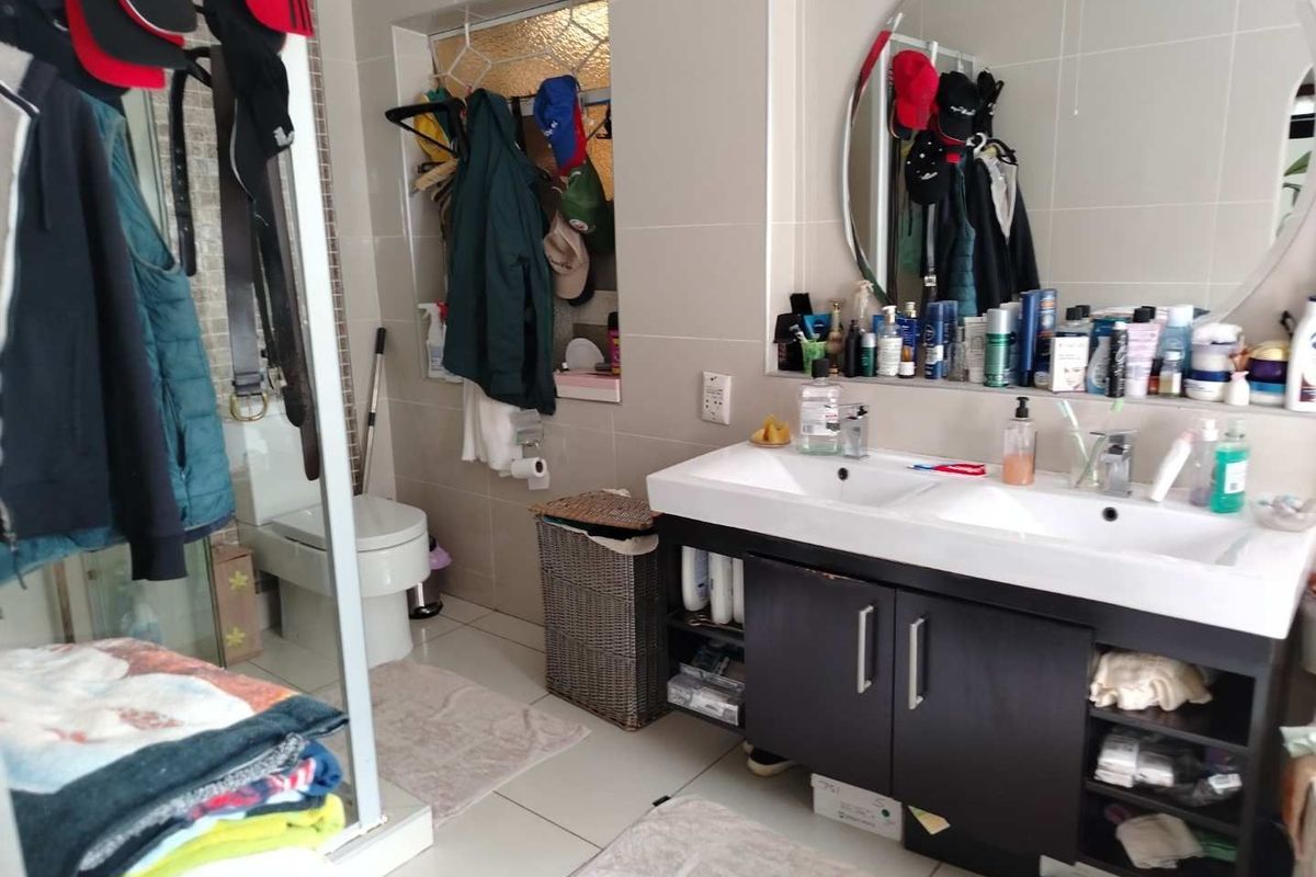 A functional bathroom featuring a double vanity with dark cabinetry, a large wall-mounted mirror, and a separate toilet area with tiled finishes.