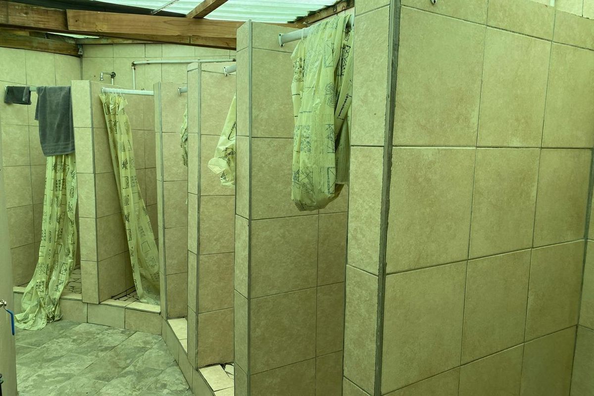 Communal shower facility featuring multiple tiled cubicles with basic plumbing fixtures and a translucent corrugated roof structure.