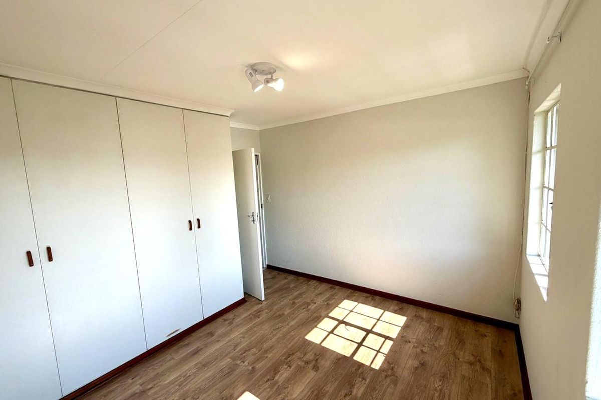 A bright, empty bedroom featuring wood-look laminate flooring, built-in white cabinetry, and a window allowing natural light.