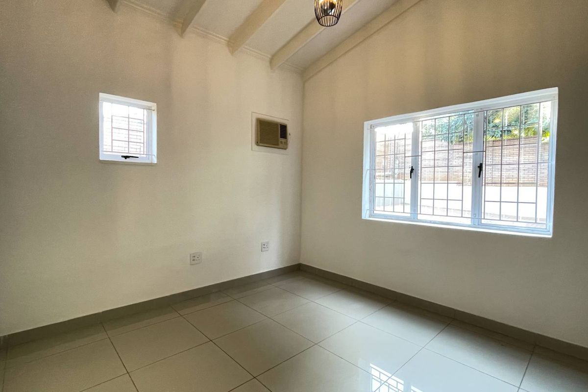 A bright, empty bedroom featuring tiled floors, exposed ceiling beams, and an integrated air conditioning unit, offering a clean and neutral living space.