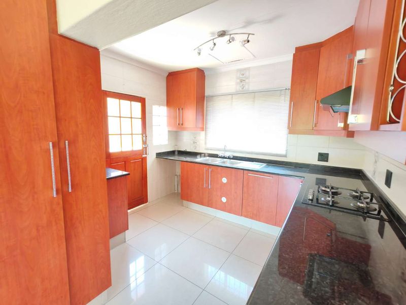 A functional kitchen featuring laminate cabinetry, granite countertops, a gas hob with extractor fan, and tiled flooring with direct access to the exterior.