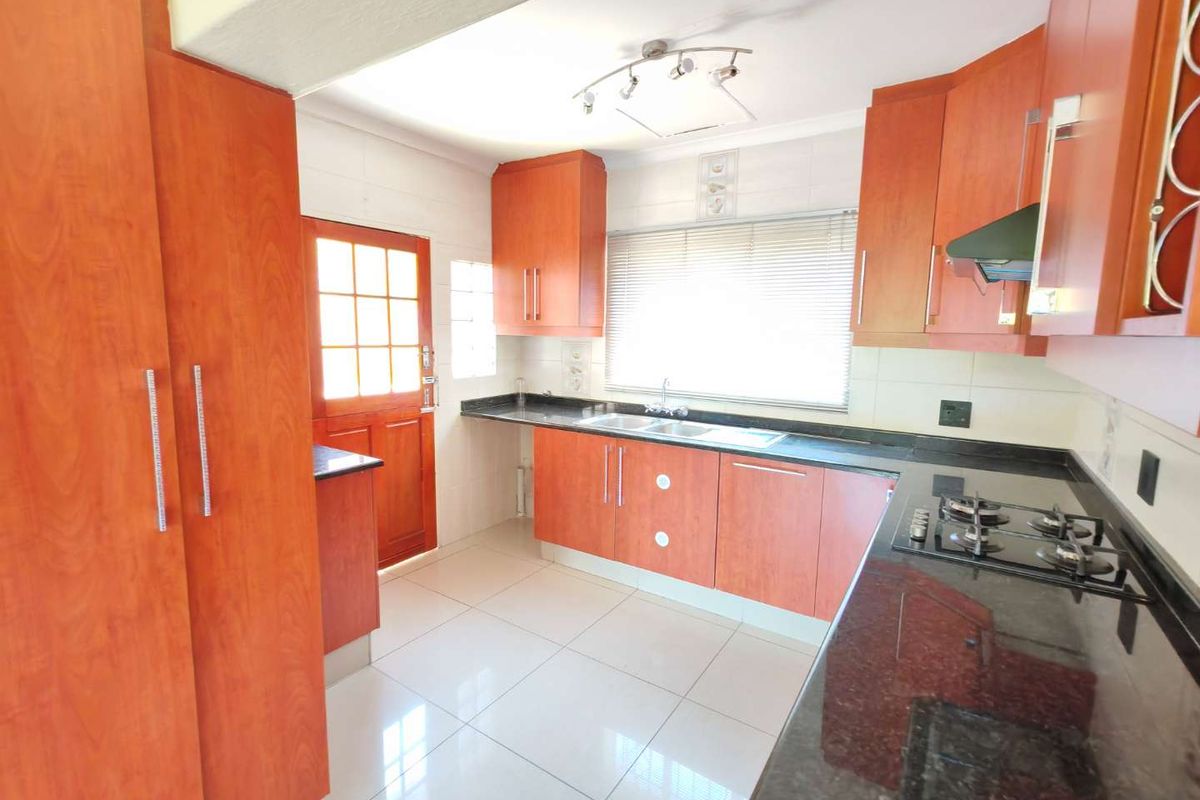 A functional kitchen featuring laminate cabinetry, granite countertops, a gas hob with extractor fan, and tiled flooring with direct access to the exterior.