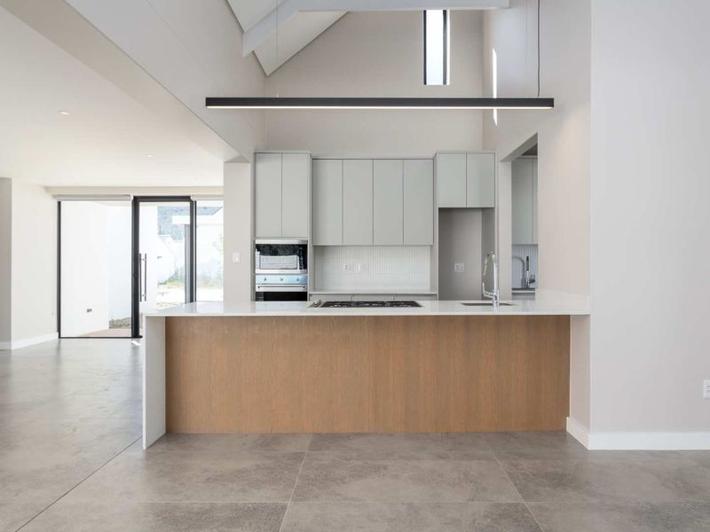 Modern open-plan kitchen featuring a central island, stone countertops, built-in oven, gas hob, and high vaulted ceilings with natural light.