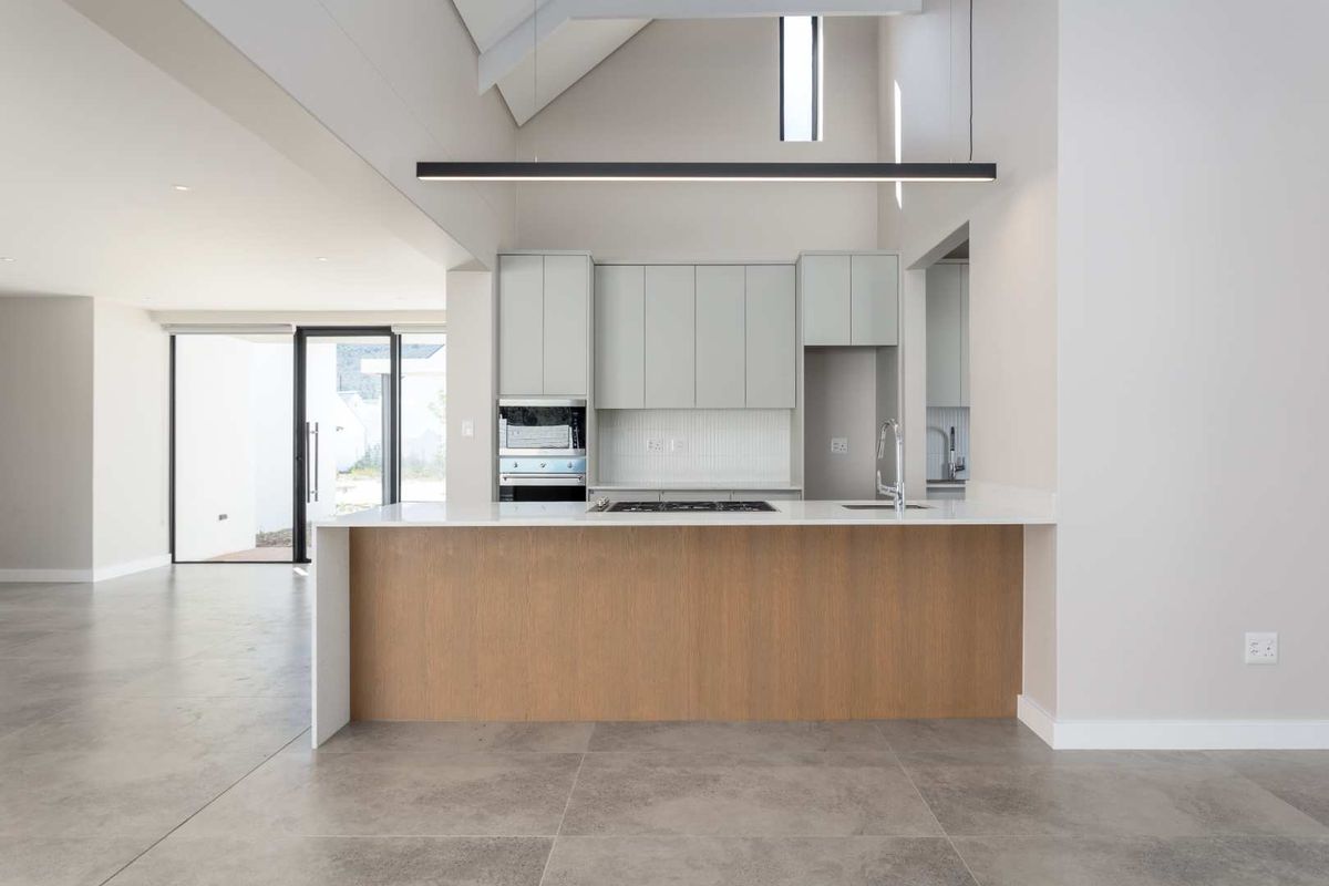 Modern open-plan kitchen featuring a central island, stone countertops, built-in oven, gas hob, and high vaulted ceilings with natural light.