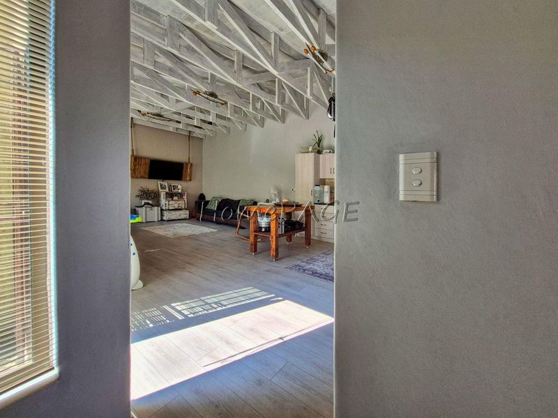 Spacious open-plan living area featuring high exposed timber roof trusses and modern laminate flooring, viewed from an adjacent doorway.
