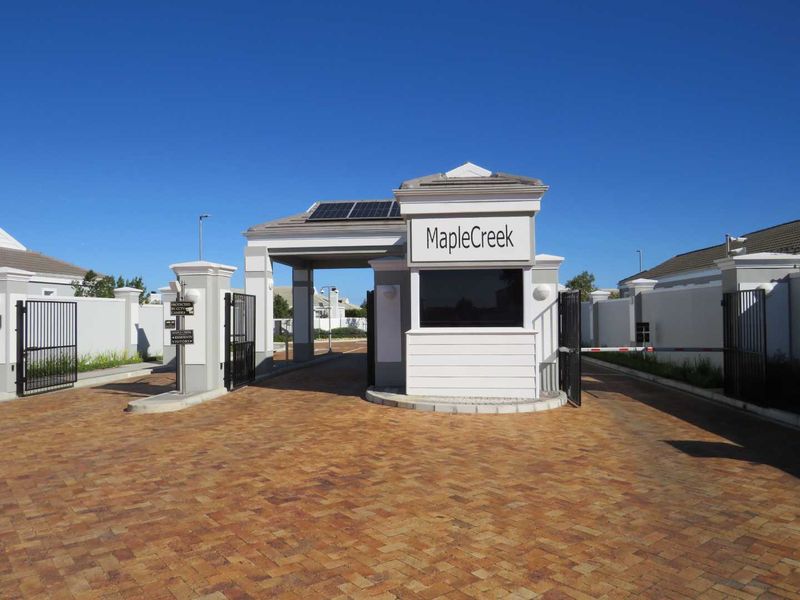 The secure entrance gate and guard house of MapleCreek estate, featuring paved driveway access, perimeter walls, and solar-powered infrastructure.