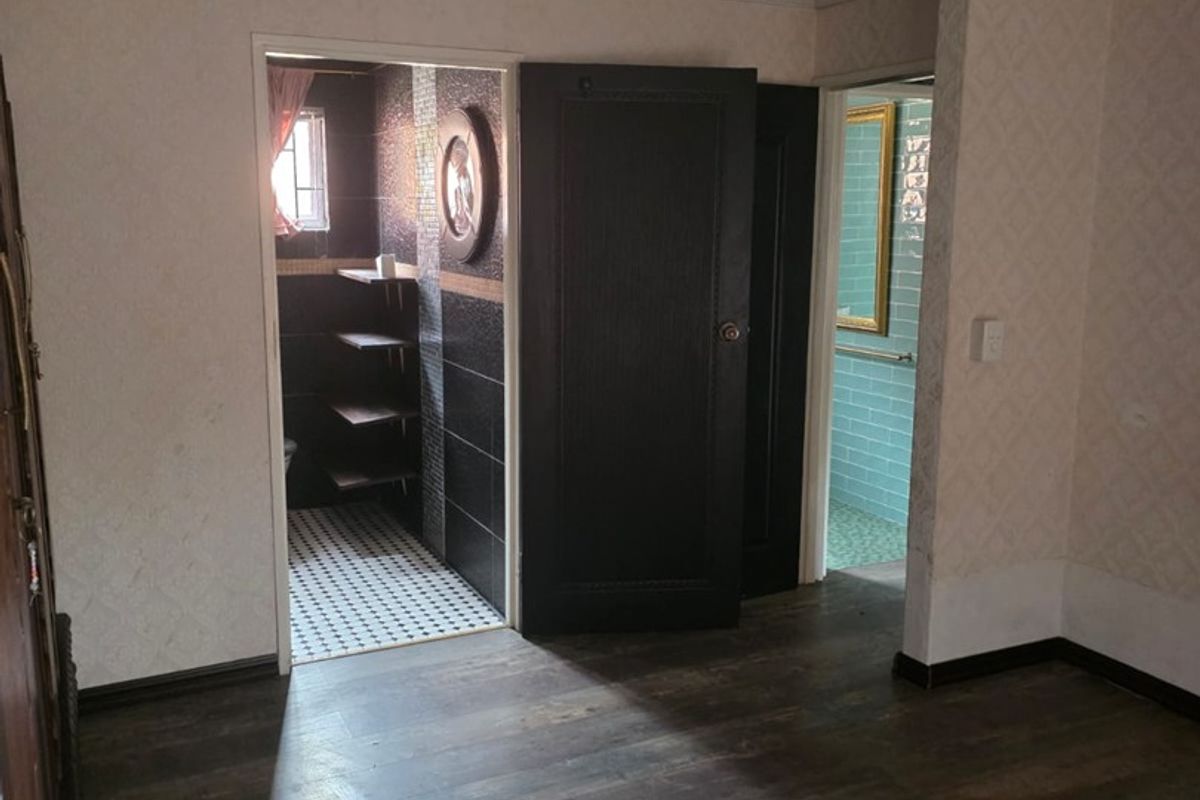 An empty bedroom featuring dark laminate flooring, crown molding, and recessed lighting, with direct access to two separate tiled bathroom areas.