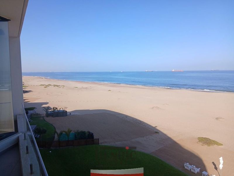A scenic elevated view overlooking the sandy beach and ocean, captured from a private balcony with a glass balustrade.