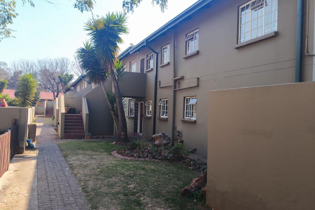Rear view of the townhouse complex featuring a paved walkway, communal garden area, and external staircase access to upper-level units.