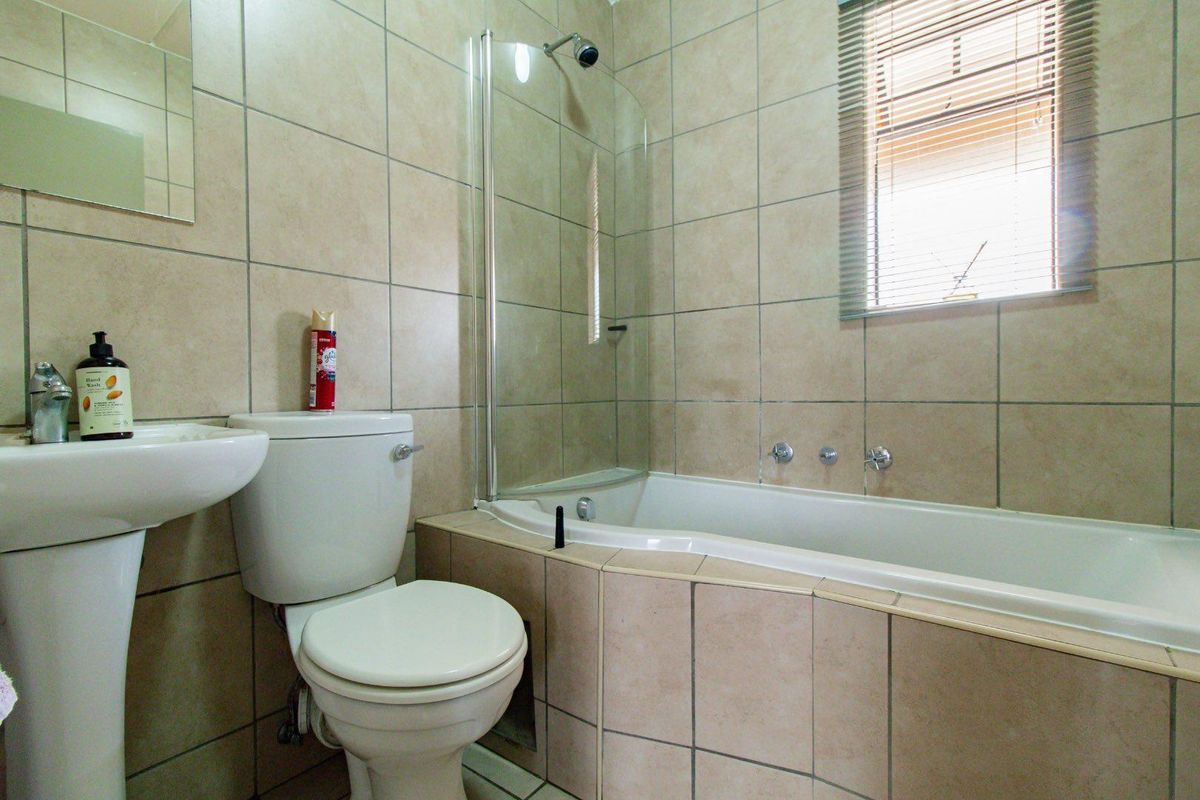 A functional bathroom featuring a pedestal basin, toilet, and a bathtub with a glass shower screen, finished with neutral wall tiling.