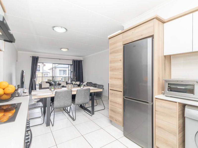 Modern open-plan kitchen and dining area featuring light wood cabinetry, tiled flooring, and direct access to a balcony through sliding glass doors.