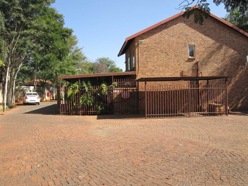 Exterior view of a face brick apartment building featuring a paved driveway, metal security fencing, and a covered carport area.