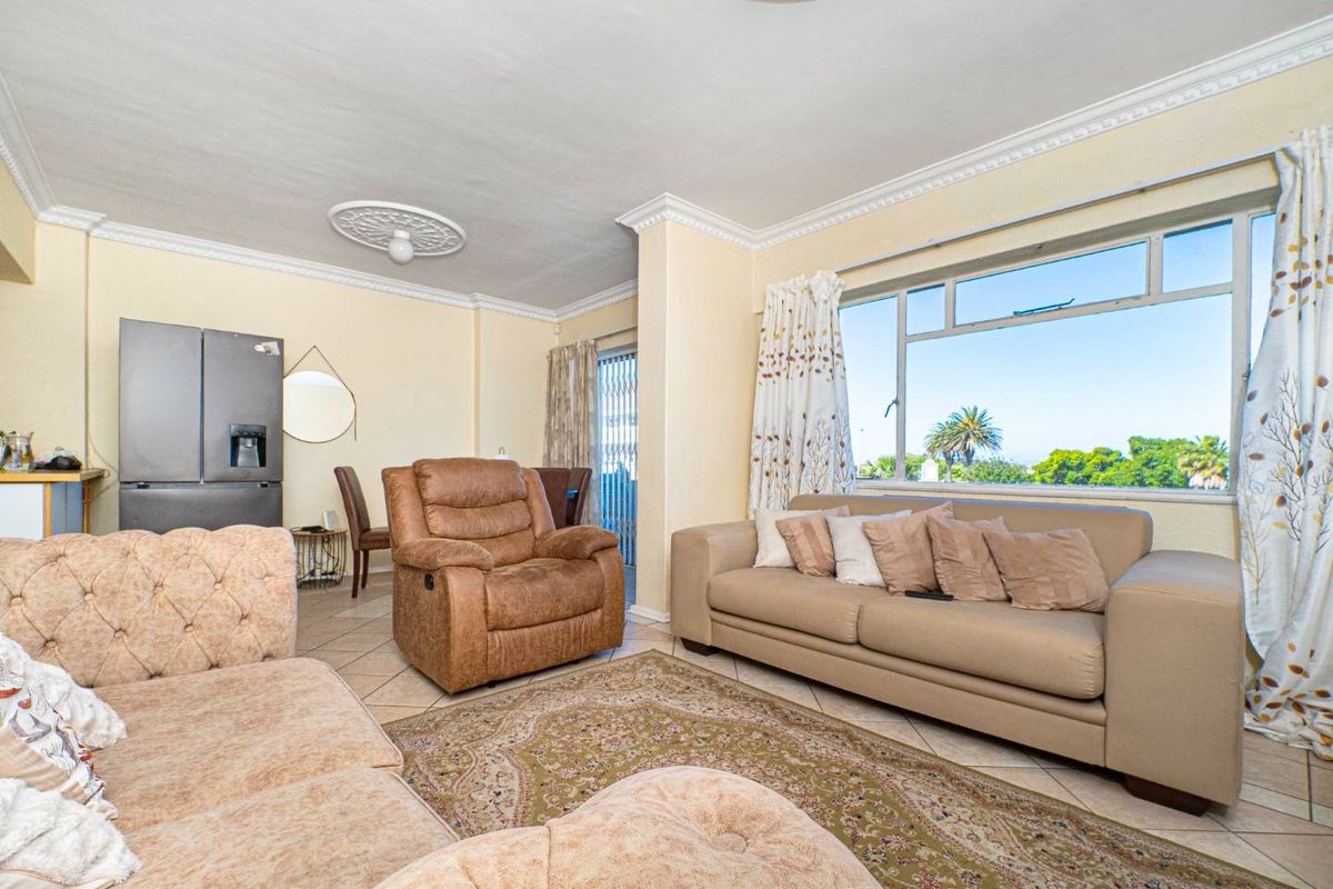 A spacious living room featuring tiled flooring, decorative ceiling roses, and large windows providing natural light and outdoor views.