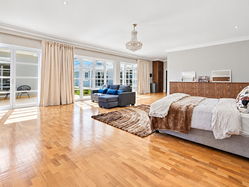 Spacious bedroom featuring warm parquet flooring, elegant crown molding, a crystal chandelier, and large glass sliding doors providing abundant natural light and patio access.