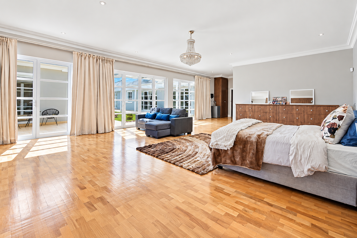 Spacious bedroom featuring warm parquet flooring, elegant crown molding, a crystal chandelier, and large glass sliding doors providing abundant natural light and patio access.