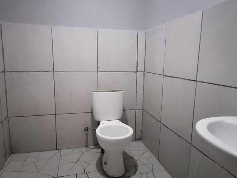 A basic bathroom featuring a standard toilet and washbasin with tiled walls and flooring, currently in need of cosmetic updates and repairs.