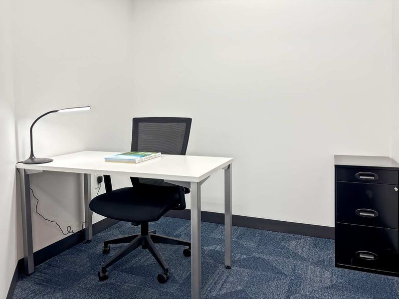 A clean, functional office space featuring blue carpet flooring and neutral walls, suitable for a professional work environment.