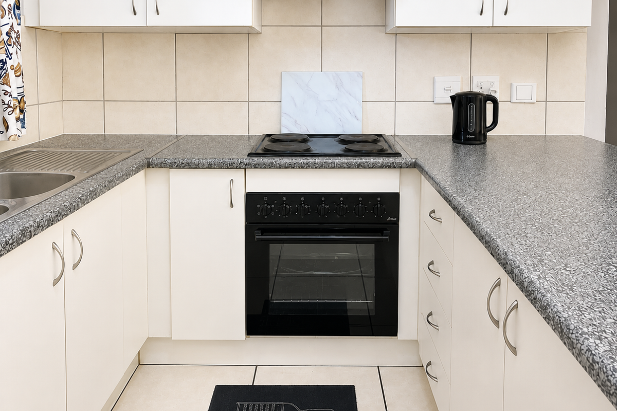 A functional kitchen featuring built-in cabinetry, a black electric oven and hob, stainless steel sink, and neutral tiled backsplash and flooring.