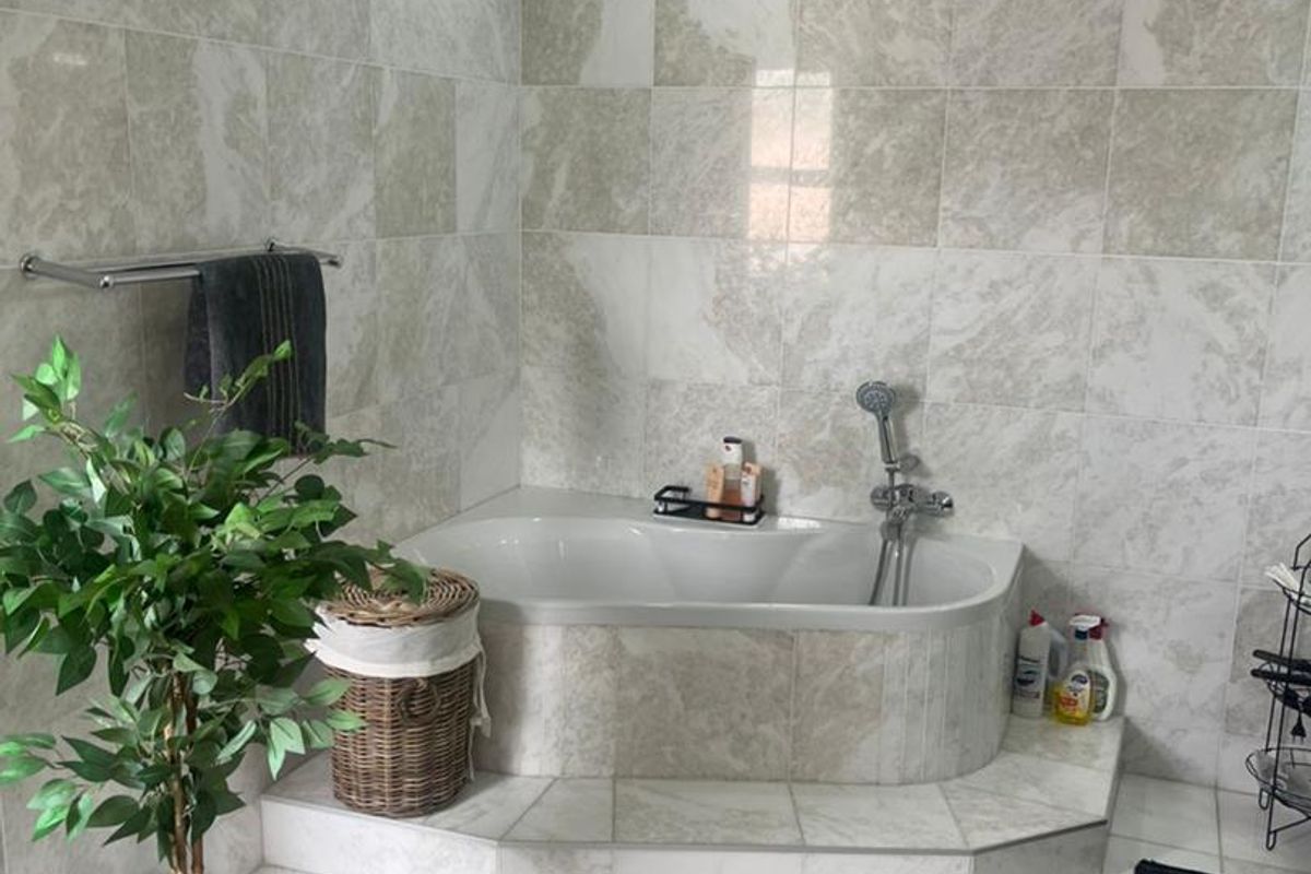 A bathroom featuring a built-in bathtub with a handheld shower mixer, complemented by marble-style wall tiles and a tiled floor.