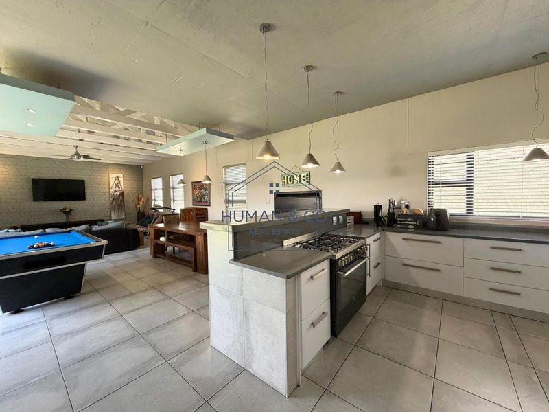 Spacious open-plan living area featuring a modern kitchen with gas stove, stone countertops, and exposed ceiling beams, seamlessly flowing into the lounge and dining space.