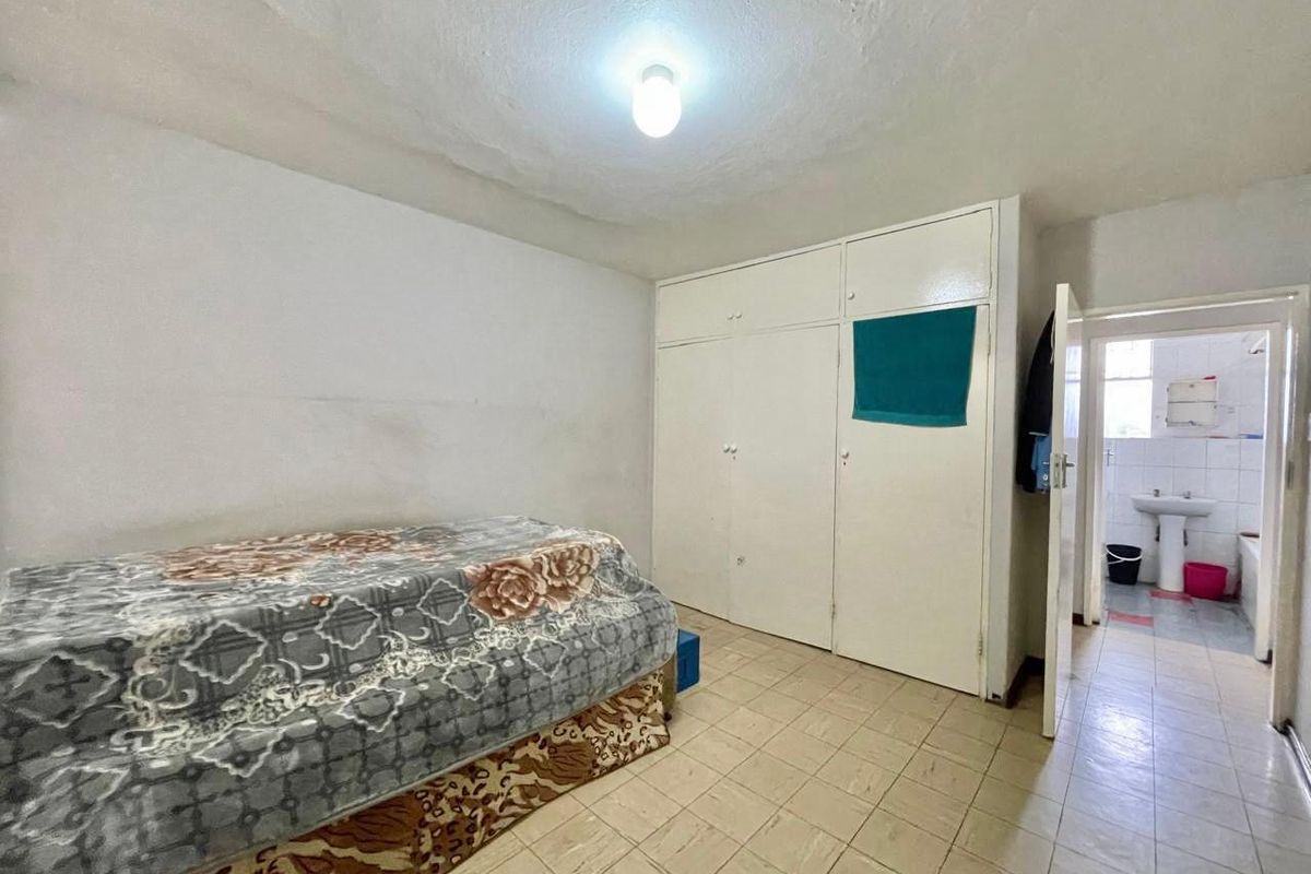 A bedroom featuring built-in cupboards and tiled flooring, with an adjoining bathroom visible through the doorway.