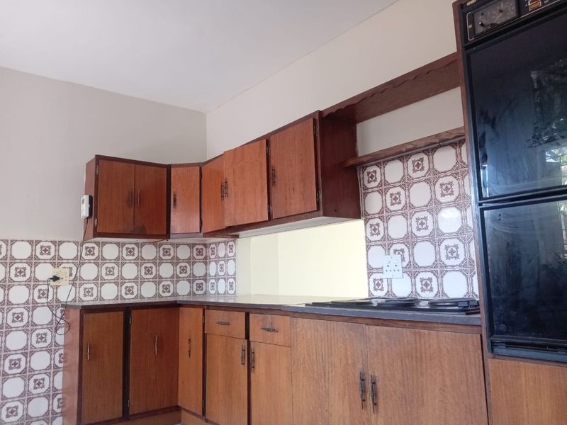 A dated kitchen featuring original wooden cabinetry, built-in oven, electric hob, and vintage patterned wall tiles, offering significant potential for a modern renovation.