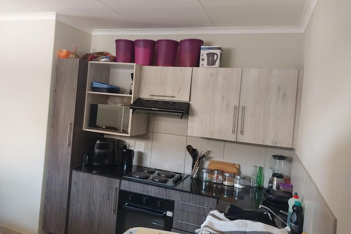 A functional kitchen featuring wood-look cabinetry, granite countertops, a built-in electric hob, oven, and extractor fan with a tiled backsplash.