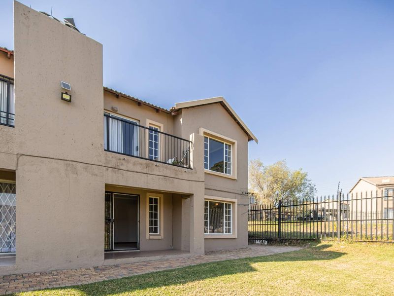 Rear view of the apartment building featuring a paved patio area, a balcony with metal railings, and a private garden enclosed by security fencing.
