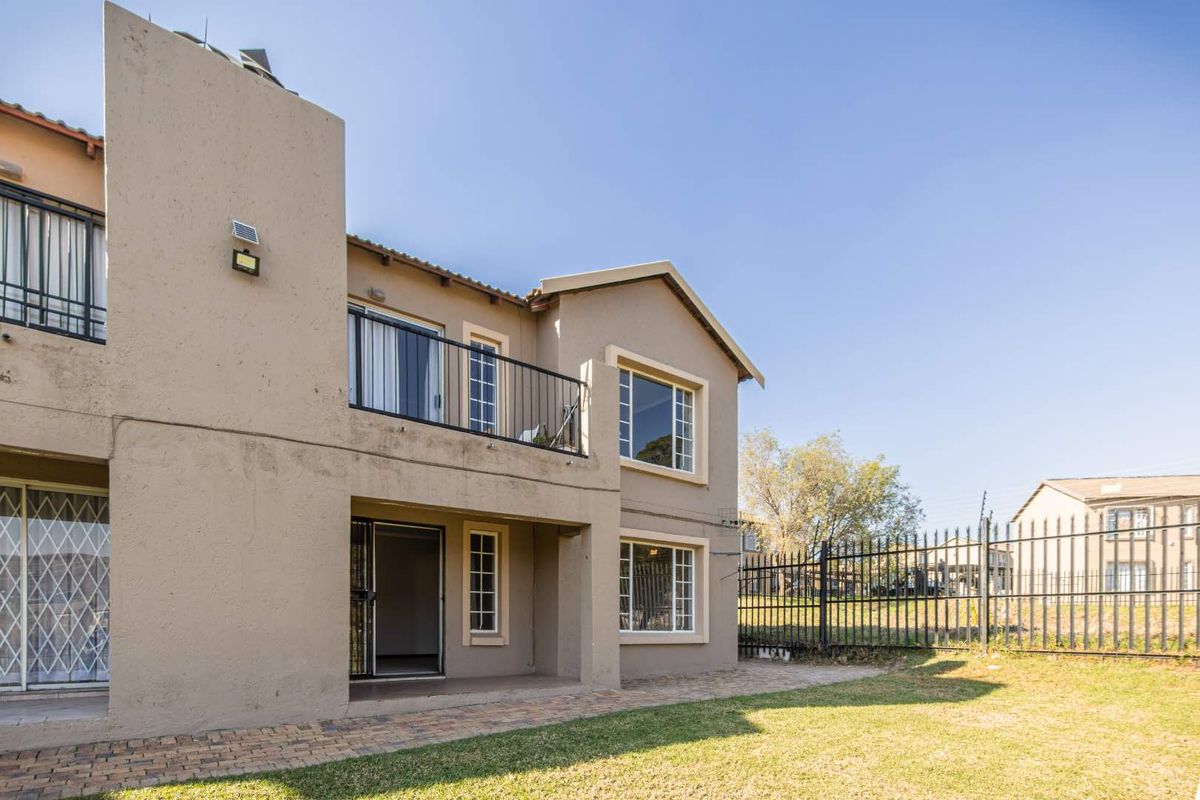 Rear view of the apartment building featuring a paved patio area, a balcony with metal railings, and a private garden enclosed by security fencing.