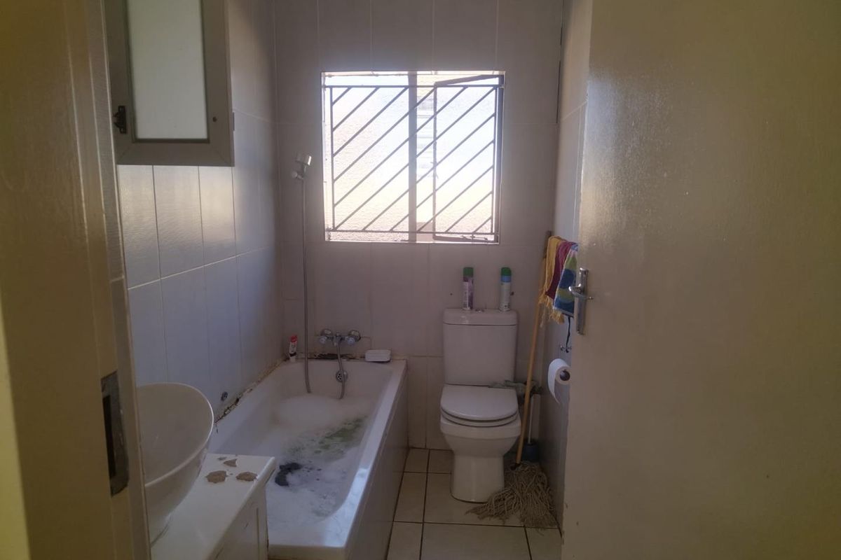 A compact bathroom featuring a built-in bathtub with shower mixer, a standard toilet, and a vanity basin with tiled walls and flooring.