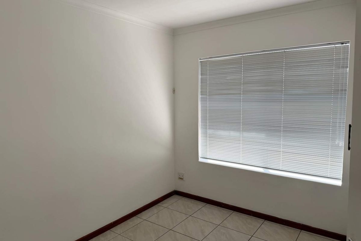 A clean, empty bedroom featuring neutral tiled flooring, white walls, and fitted venetian blinds, offering a versatile space ready for personalization.